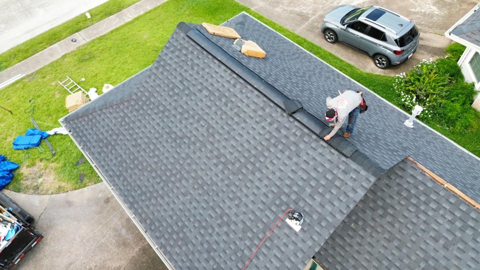 Roofer working along the ridge of a shingle roof